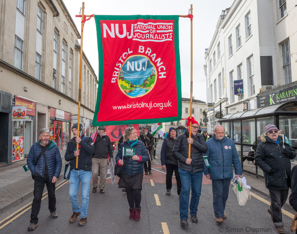 27/01/2024; Cheltenham, UK. Members of the NUJ's South West England branch carry the Bristol banner with other trade unions and supporters marching to mark the 40th anniversary of the banning of trade union rights at GCHQ